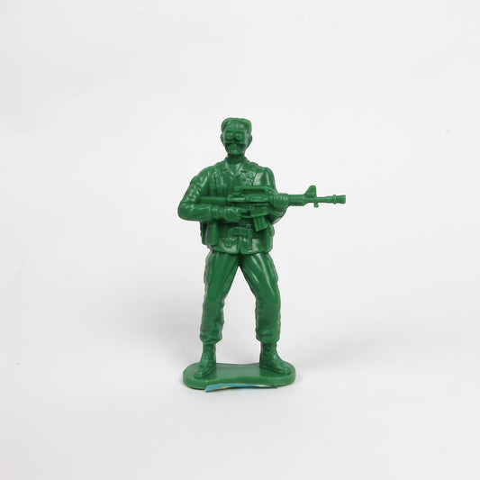 Outrageous Art green plastic toy soldier figurine holding a rifle with goggles and utility belt on a white background