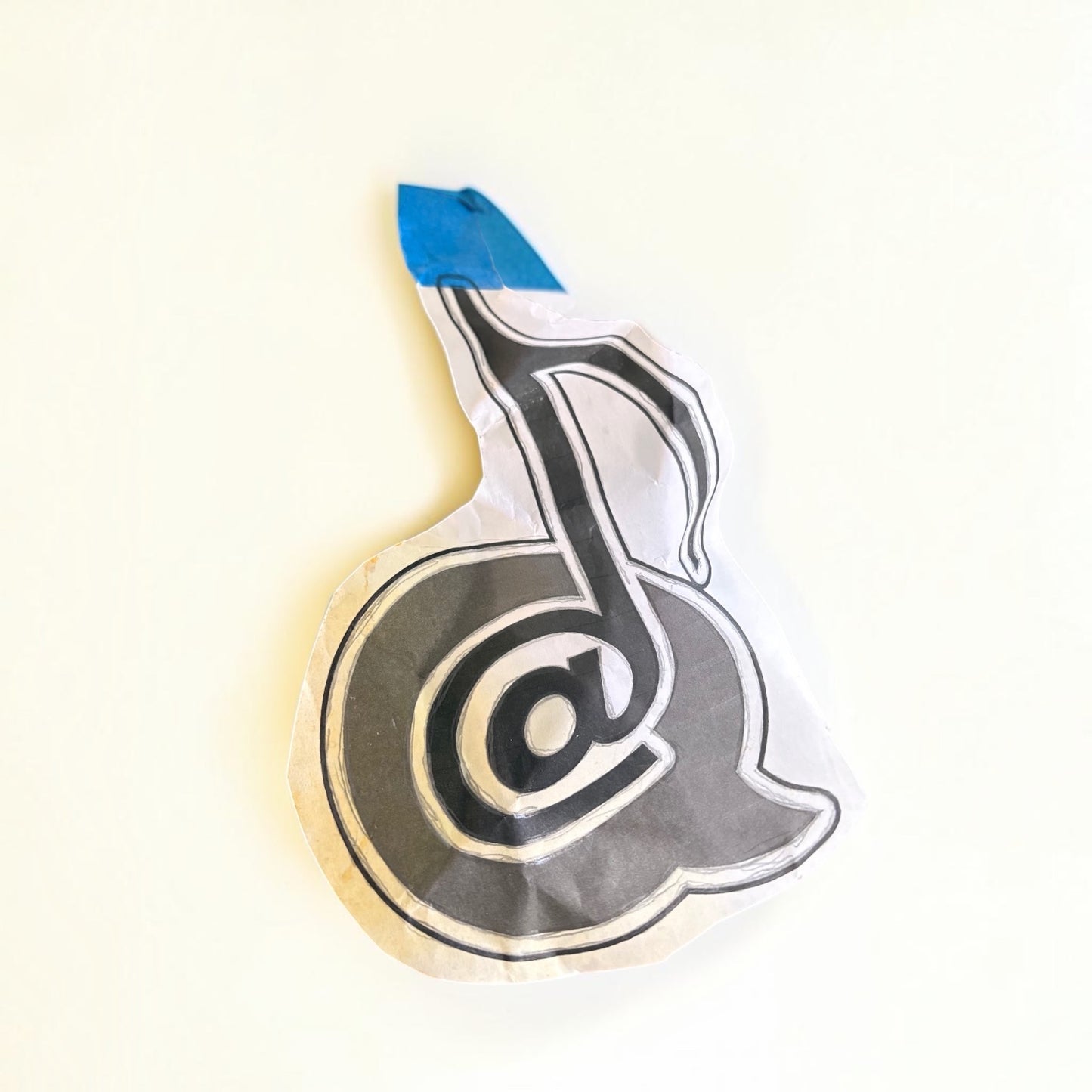 Outrageous Art hand-drawn paper cutout featuring a monochromatic musical note and at-symbol fusion design.
