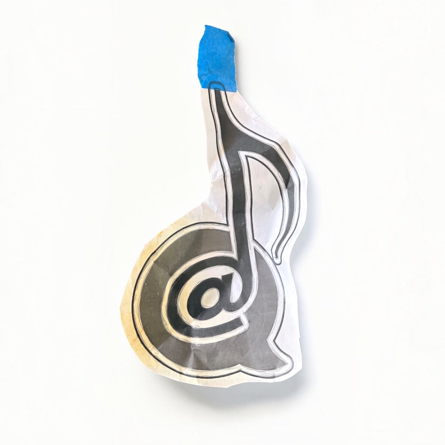 Outrageous Art hand-drawn paper cutout featuring a musical note and at-symbol fusion design on a wooden table.