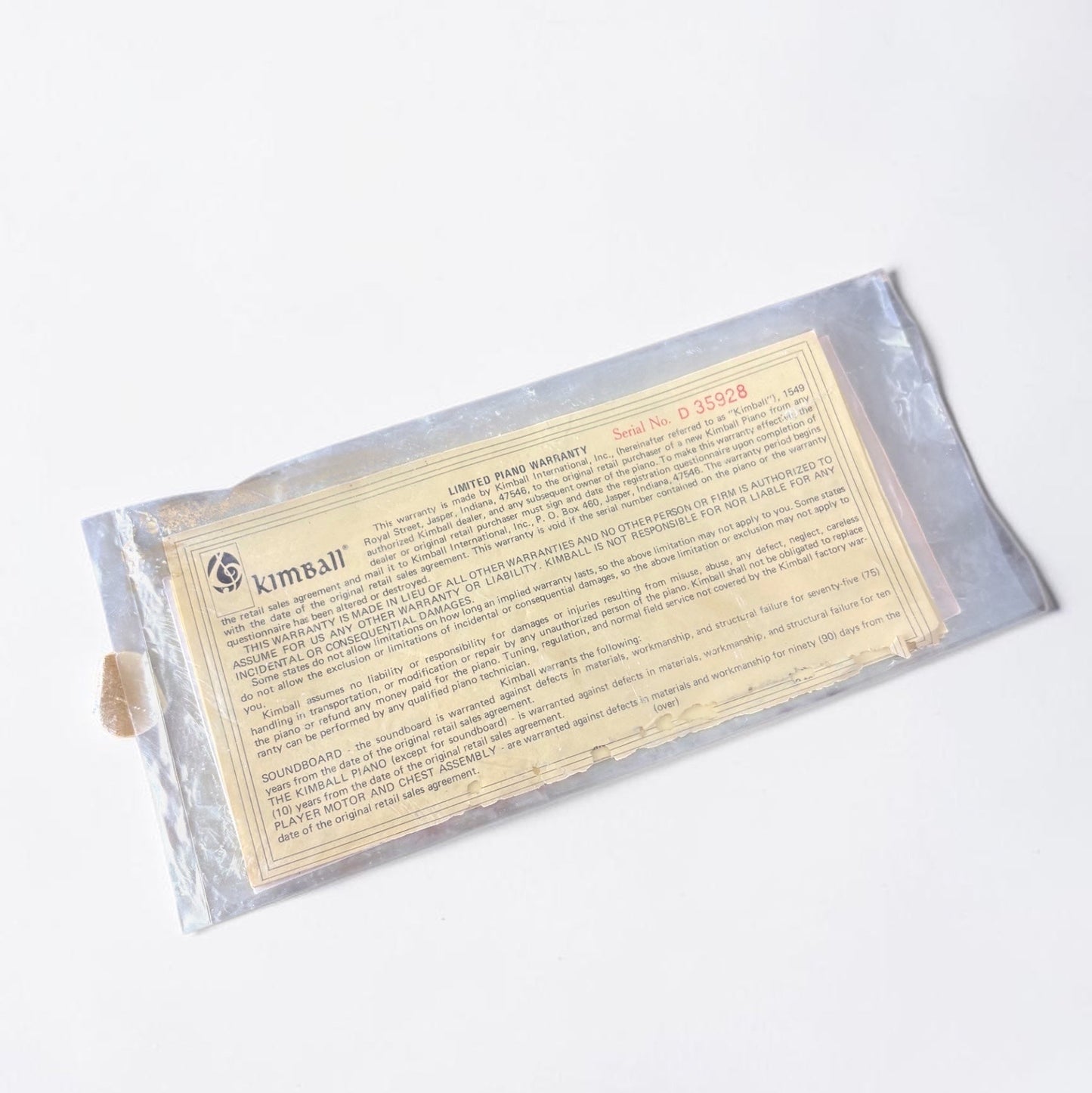Outrageous Art vintage Kimball Piano limited warranty document in a protective plastic sleeve on a wooden surface.